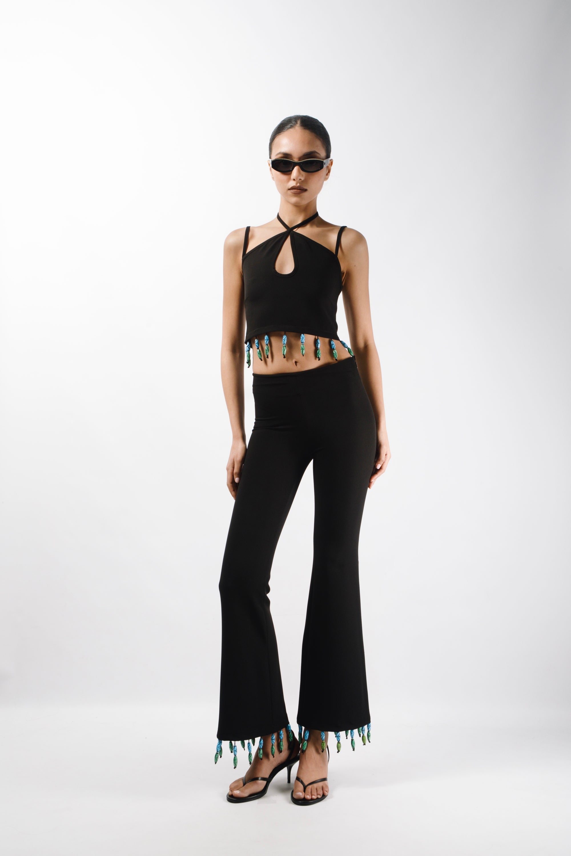 Tailored pants featuring mid rise waist and flared leg, embelished with bead fringes on the hem - front